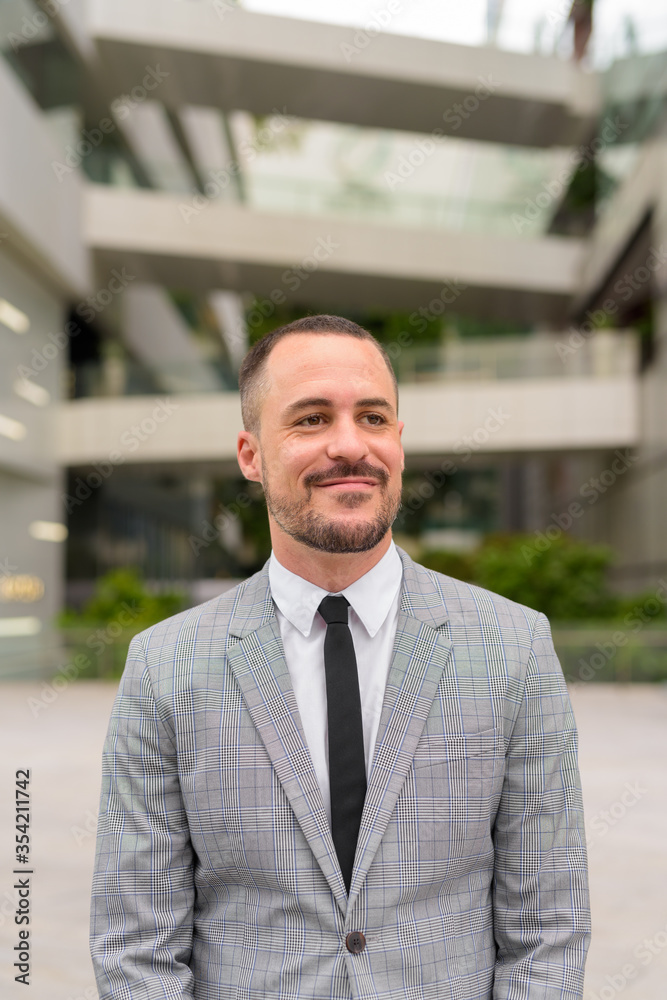 Handsome Hispanic bald bearded businessman thinking in the city outdoors Handsome Hispanic bald bearded businessman thinking in the city outdoors