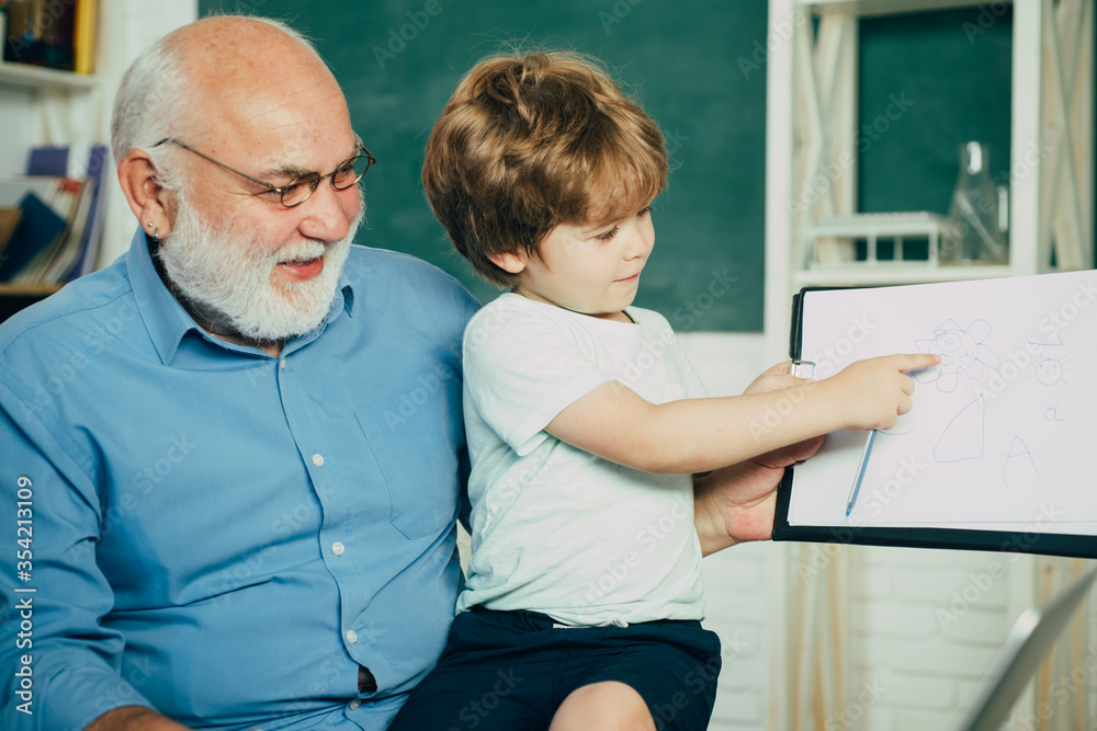 Fototapeta premium Portrait of grandfather and grandson on blackboard in classroom. Kid with old teacher learning in class on background of blackboard. Father and son.