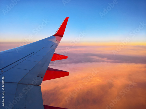Airplane wing with red winglets at sunset over clouds