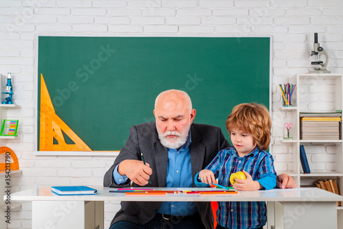 Mature man teacher and pupil on balckboard background. Senior teacher in classroom with elementary school kid. Science education concept. photo