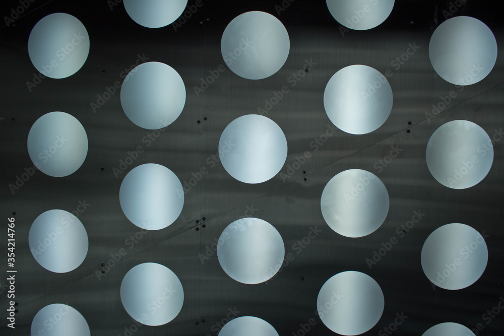 Metal surface with luminous round holes in gray metallic tones. It can be used as a background for futuristic designs or as an idea for a wall in a nightclub.
