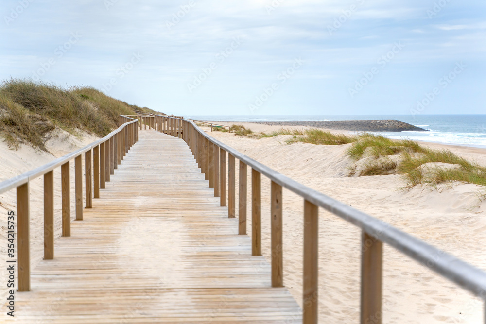 Wooden path at over sand dunes with ocean view. Wooden footbridge of Costa Nova beach in Aveiro, Portugal. Wooden path at over sand dunes with ocean view. Wooden footbridge of Costa Nova beach in Aveiro, Portugal.