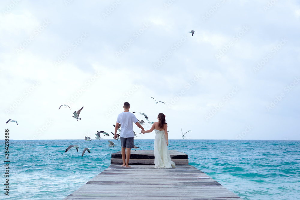 A man and a woman walk on the pier by the sea and look at the horizon.
