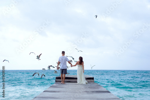 A man and a woman walk on the pier by the sea and look at the horizon.