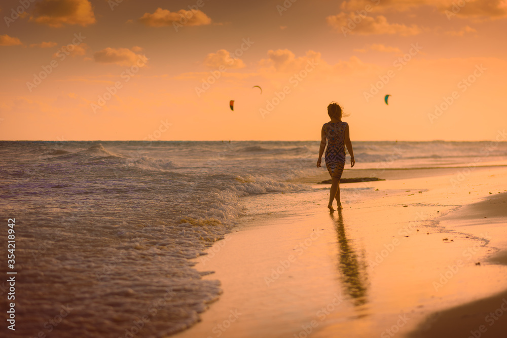 The silhouette of a woman on the beach and against the backdrop of the sunset.