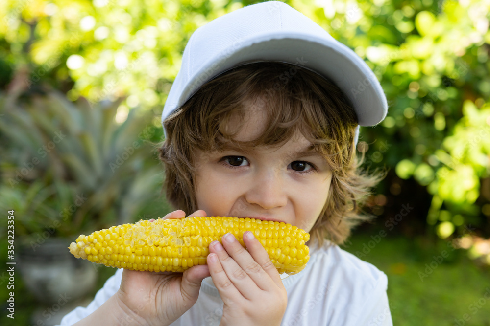 Child in the garden, corn - lovely boy eating corn on the cob in the garden. Portrait of a cute boy eating corn. Farming and autumn crops concept. Child in the garden, corn - lovely boy eating corn on the cob in the garden. Portrait of a cute boy eating corn. Farming and autumn crops concept.