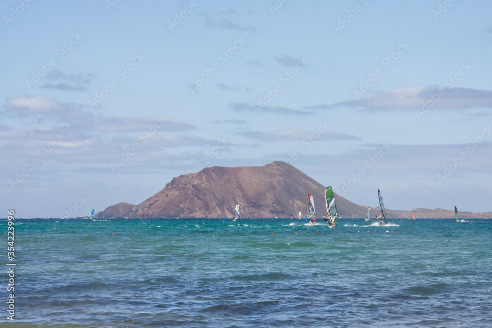Los Lobos Island from Corralejo, Fuerteventura scenic view of the volcano on IslaLos Lobos. Windsurfer and a small boat. Space left for copy text Los Lobos Island from Corralejo, Fuerteventura scenic view of the volcano on IslaLos Lobos. Windsurfer and a small boat. Space left for copy text