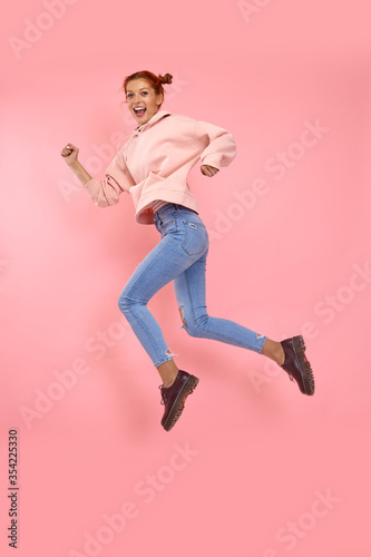 Full length body shot of incendiary cheerful emotional beautiful young woman in casual clothes jump high in a running pose on a pink background in the studio. Concept of pursuit of career and success