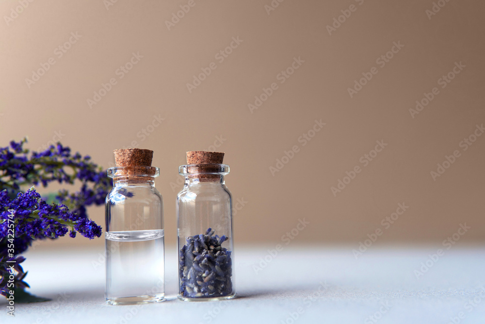 Organic aromatherapy essential oil bottle next to glass bottle dried lavender flower with artificial lavender plant with soft plain brown purple color as a background. Organic aromatherapy essential oil bottle next to glass bottle dried lavender flower with artificial lavender plant with soft plain brown purple color as a background.