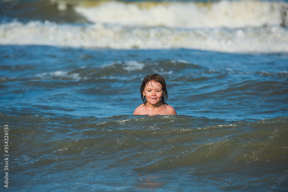 Boy at beach during summer vacation. Kid swimming in sea with wawes.