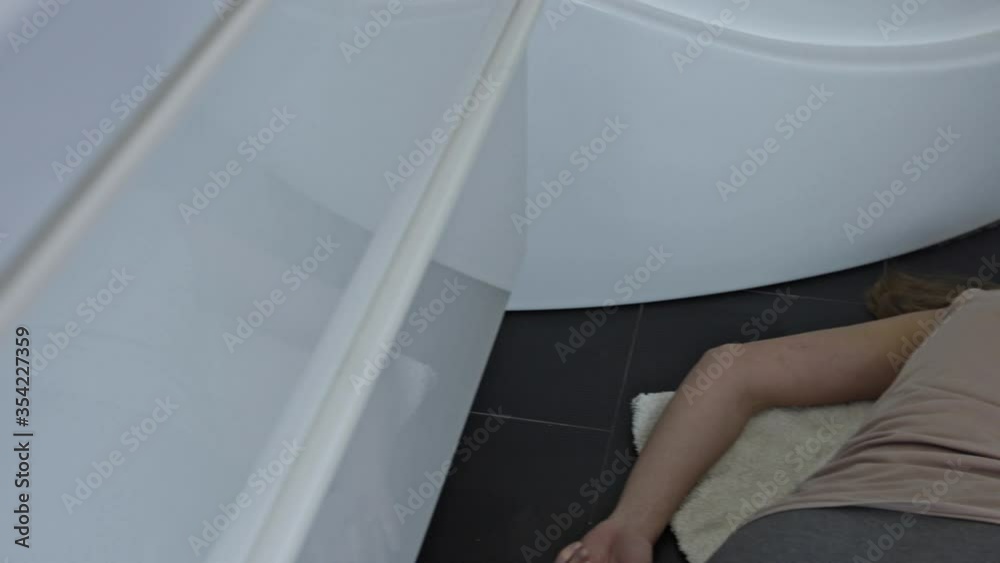 The unconscious woman lies motionless on the floor in the home bathroom.