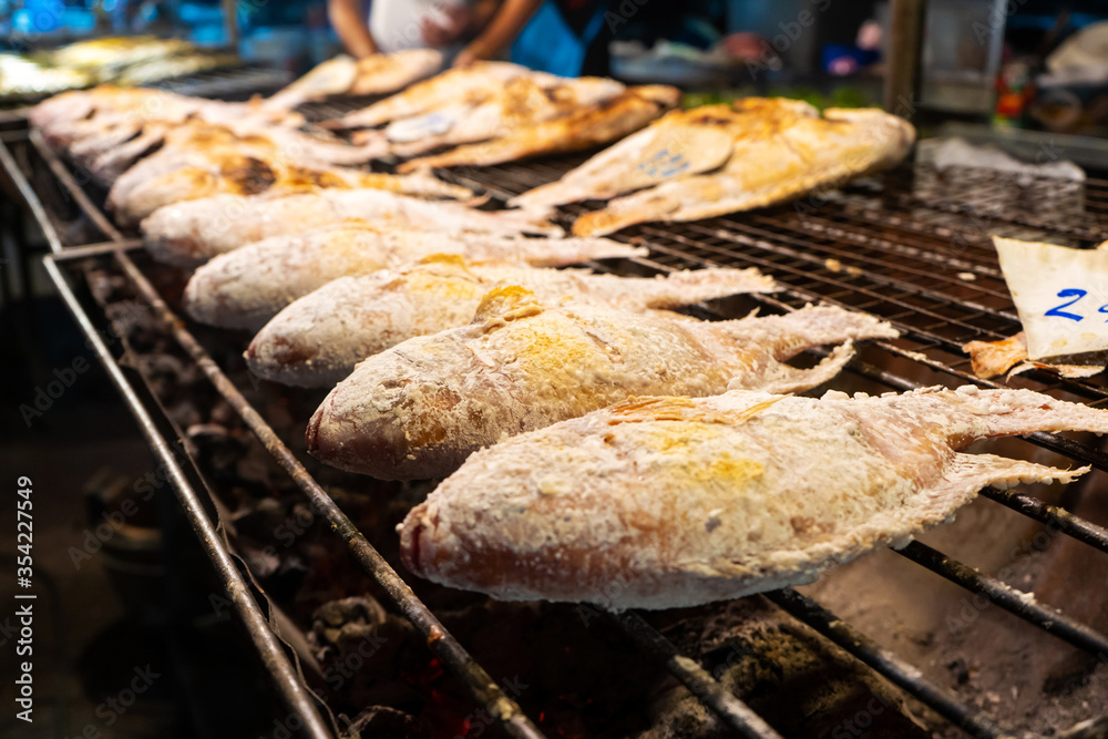 Asian food. Counter with fish in salt on the grill at a night food street market.