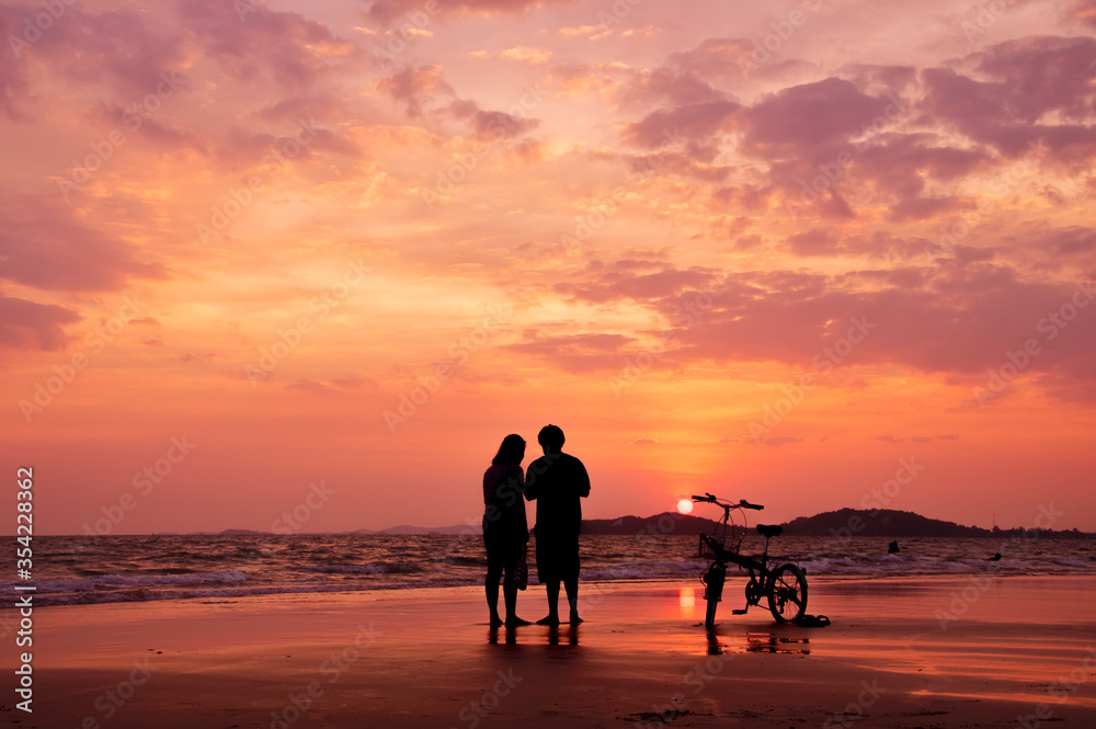 Silhouette of couple standing on the beach with dramatic sunset sky
