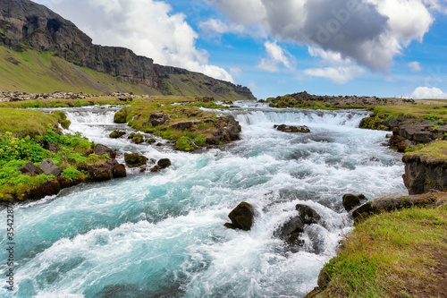 Mountains and beautiful streams in summer, with green grass and blue skies with beautiful clouds In the countryside in Iceland The picture is bright and refreshing, looks relaxed.