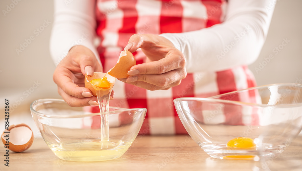 Detail of woman's hands separating egg yolks from the whites into two glass bowls Detail of woman's hands separating egg yolks from the whites into two glass bowls