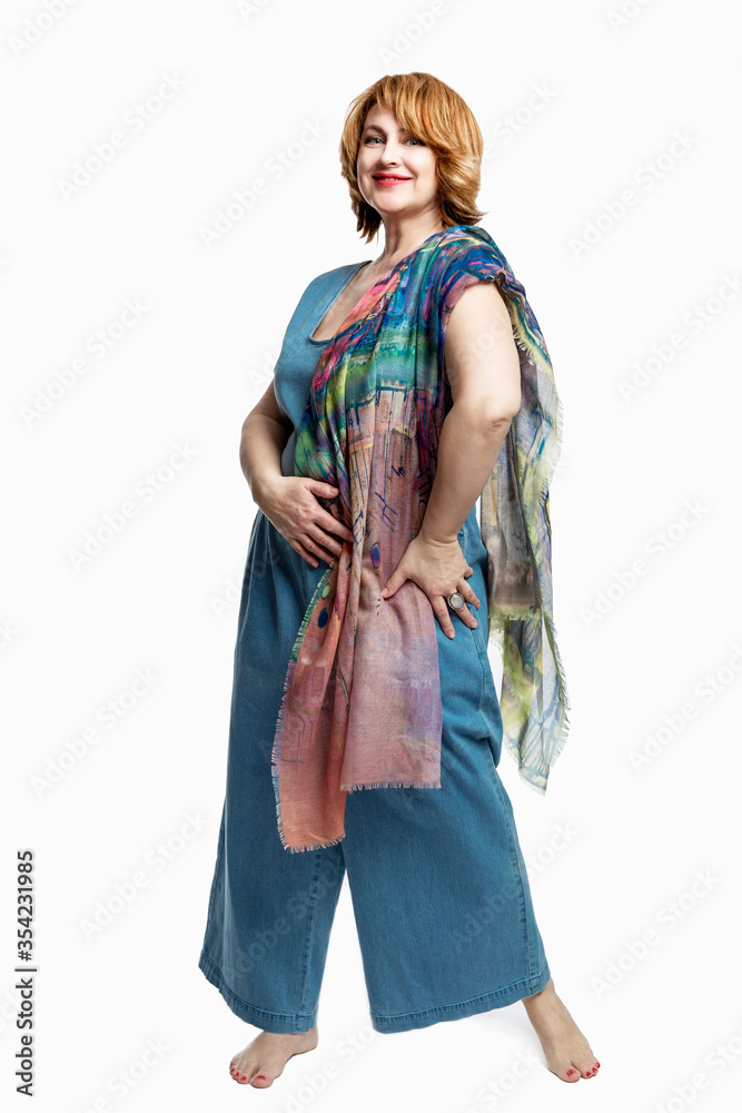 Modern woman with red hair in denim overalls barefoot. Beautiful and happy aging. Isolated on a white background. Full height. Vertical. Modern woman with red hair in denim overalls barefoot. Beautiful and happy aging. Isolated on a white background. Full height. Vertical.
