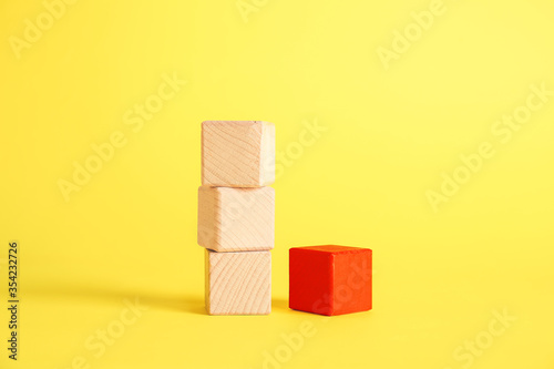 Red cube among wooden ones on color background. Concept of uniqueness