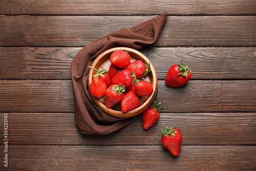 Bowl with ripe strawberry on wooden background