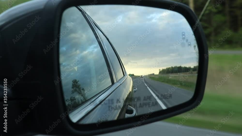 Traveling on flat straight highway looking in side view mirror at cloudscape and road, handheld Traveling on flat straight highway looking in side view mirror at cloudscape and road, handheld