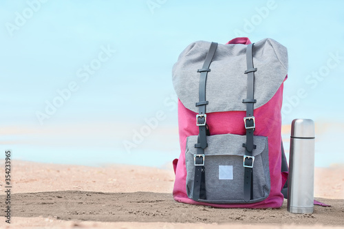 Traveler's backpack and thermos bottle near river outdoors