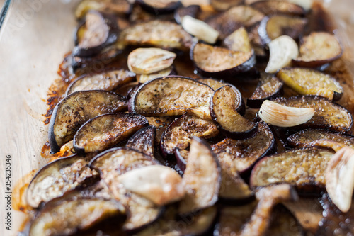 Sliced eggplants baked in oven with garlic cloves lying on glass tray ready to be eaten