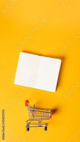 content marketing concept,top view oepn book with shopping cart on yellow desk surface.leave space for display your content.vertical background 9-16 ratio for advertise on mobile media