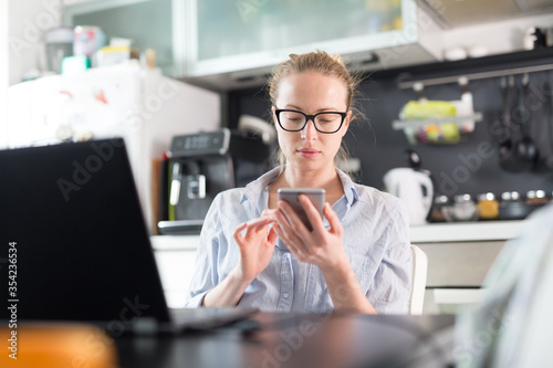 Stay at home and social distancing. Woman in her casual home clothing working remotly from kitchen dining table. Video chatting using social media with friend, family, business clients or partners. photo