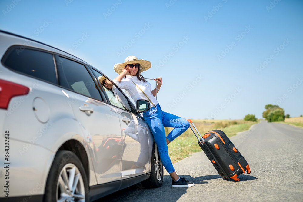 Pretty girl with suitcase standing near car and wiat for her dreaming trip. - obrazy, fototapety, plakaty 