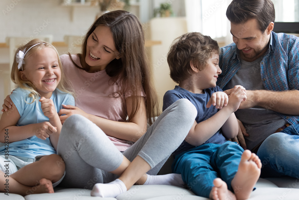 Happy young parents have fun play tickle with overjoyed little preschooler children, smiling mother and father feel playful engaged in funny game with small daughter and son entertain at home Happy young parents have fun play tickle with overjoyed little preschooler children, smiling mother and father feel playful engaged in funny game with small daughter and son entertain at home