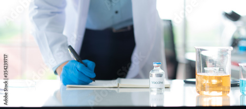 Professional Asian scientist or researcher man in work coat uniform writing a result of experiment and holding colorful sample in test tube in science lab