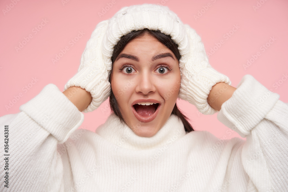 Portrait of young agitated brown haired woman holding raised hands on her head while looking amazedly at camera with wide mouth opened, isolated over pink background Portrait of young agitated brown haired woman holding raised hands on her head while looking amazedly at camera with wide mouth opened, isolated over pink background