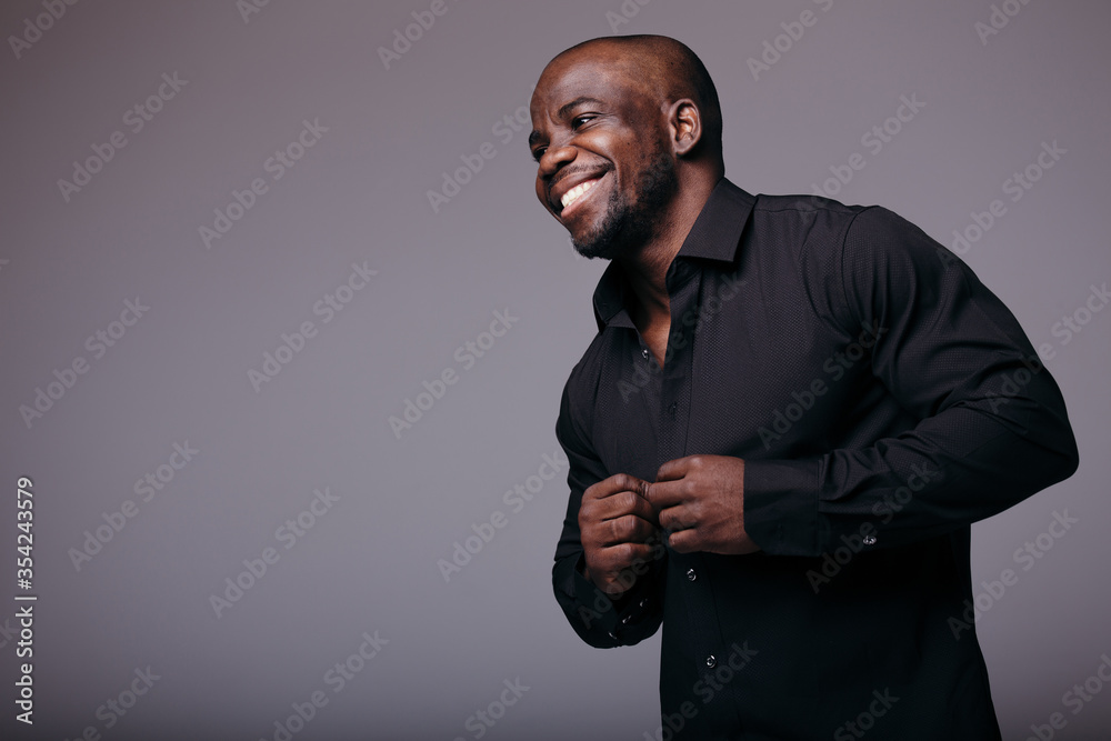 African bald funny man smiles and buttons his shirt and looks ahead. A man  wearing a black shirt. Stock Photo | Adobe Stock