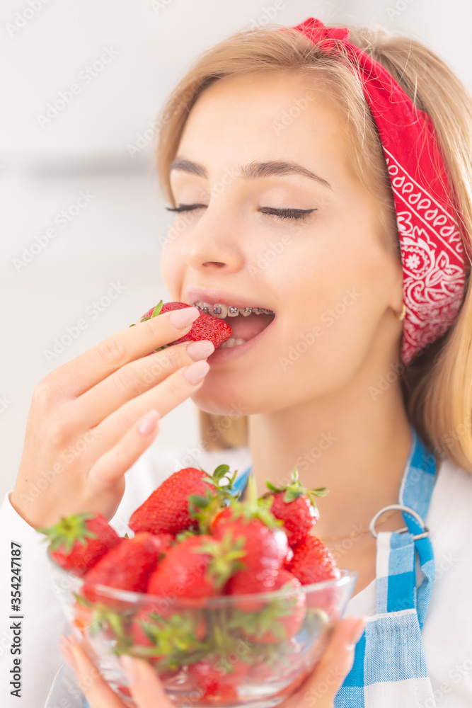 Beuatiful young woman enjoying the taste of a bite from a fresh strawberry with a bowl of more fruits in front of her Beuatiful young woman enjoying the taste of a bite from a fresh strawberry with a bowl of more fruits in front of her