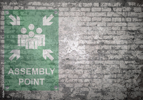 Grunge decayed faded brick wall background with assembly point sign with copy space for own text