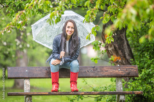 Photos Smiling pretty woman holding umbrella on her shoulder sits on a bench back-rest
