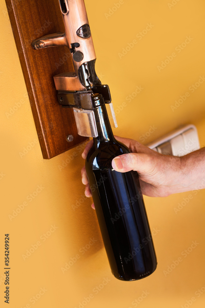 Mano de hombre sosteniendo una botella de vino y un sacacorchos anclado y  montado en la pared. Vista de frente y de cerca. Copy space Photos