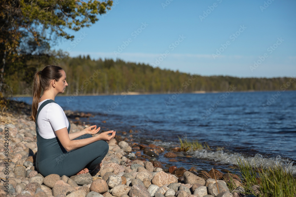 The girl does yoga on the shore of the lake.