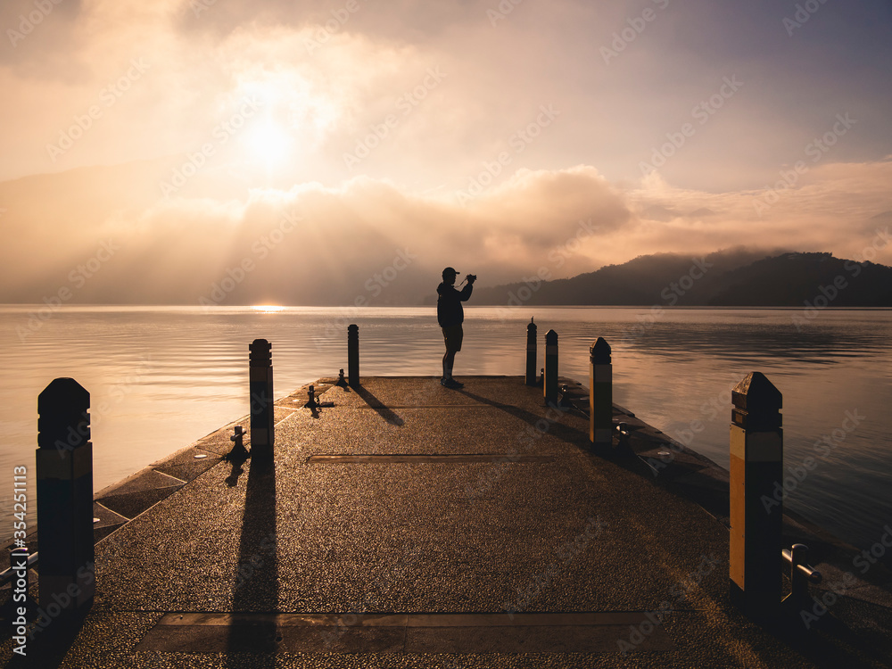 Fototapeta premium Traveler standing on Pier Lake take photo of Mountain Landscape morning scene 
