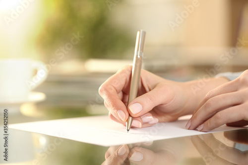 Woman hand writing on a paper on a desk at home photo