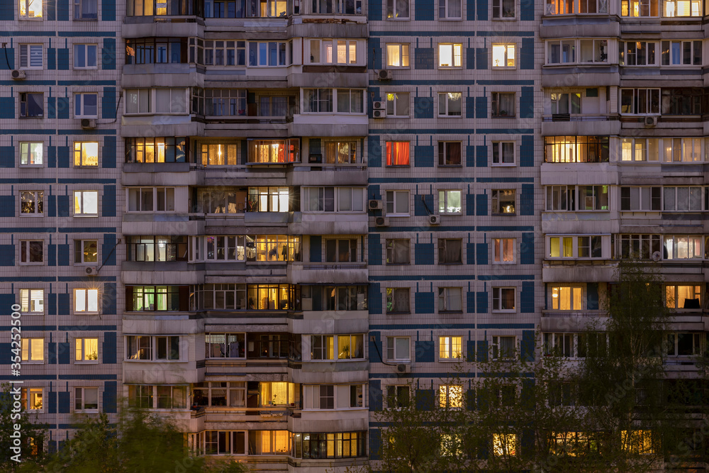 Facade of large multi-storey block residential buildinf with many bright lighting windows in apartments and balconiesю Evening view. Moscow Russia