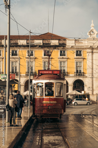 Lisbon / Portugal November 23 2019: Tram is passing by with people and yellow building at the background