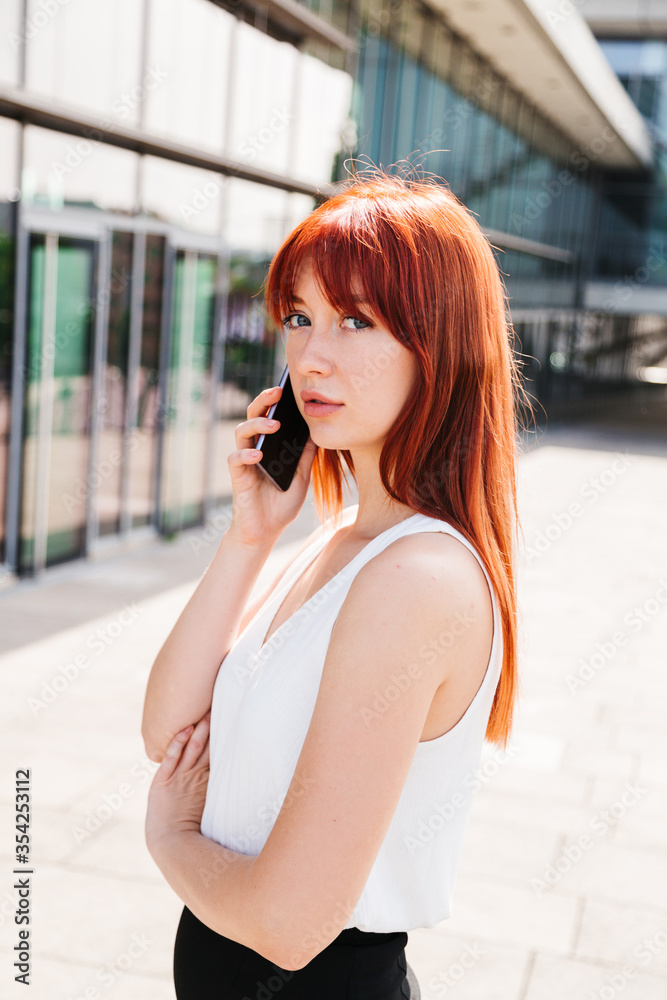 Fototapeta premium Red-haired girl talks on phone and looks at camera