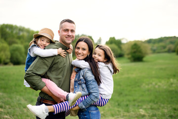 Happy family with two small daughters standing outdoors in spring nature.