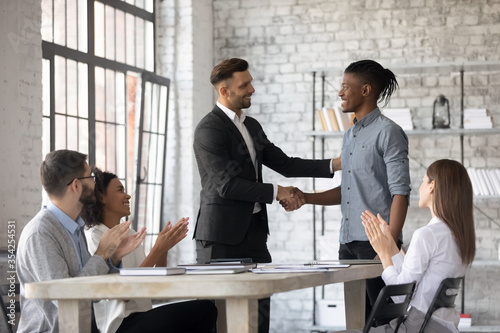 Smiling executive congratulating successful African American employee with promotion, shaking hands at corporate meeting, confident team leader greeting new member at briefing in boardroom photo