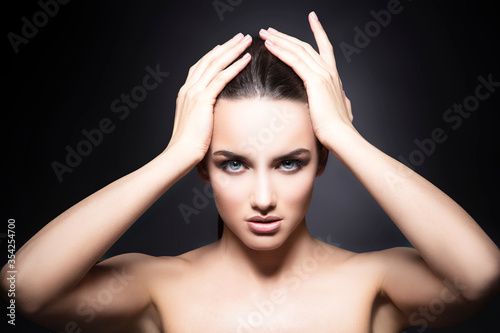 Beauty fashion model woman slick hair with hands, perfect skin, natural make-up, dark studio background