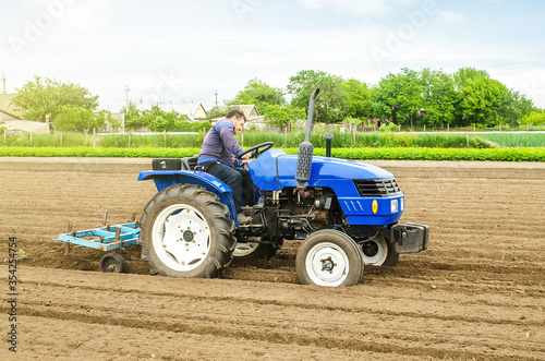 A white caucasian farmer on a tractor making rows on a farm field. Preparing the land for planting future crop plants. Cultivation of soil for planting. Agroindustry, agribusiness. Farming, farmland. photo