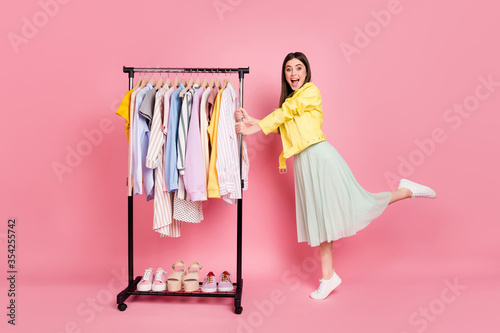 I want all this. Full length photo of pretty lady showroom fashion collection choosing clothes wear trend yellow leather jacket long skirt shoes isolated pastel pink color background