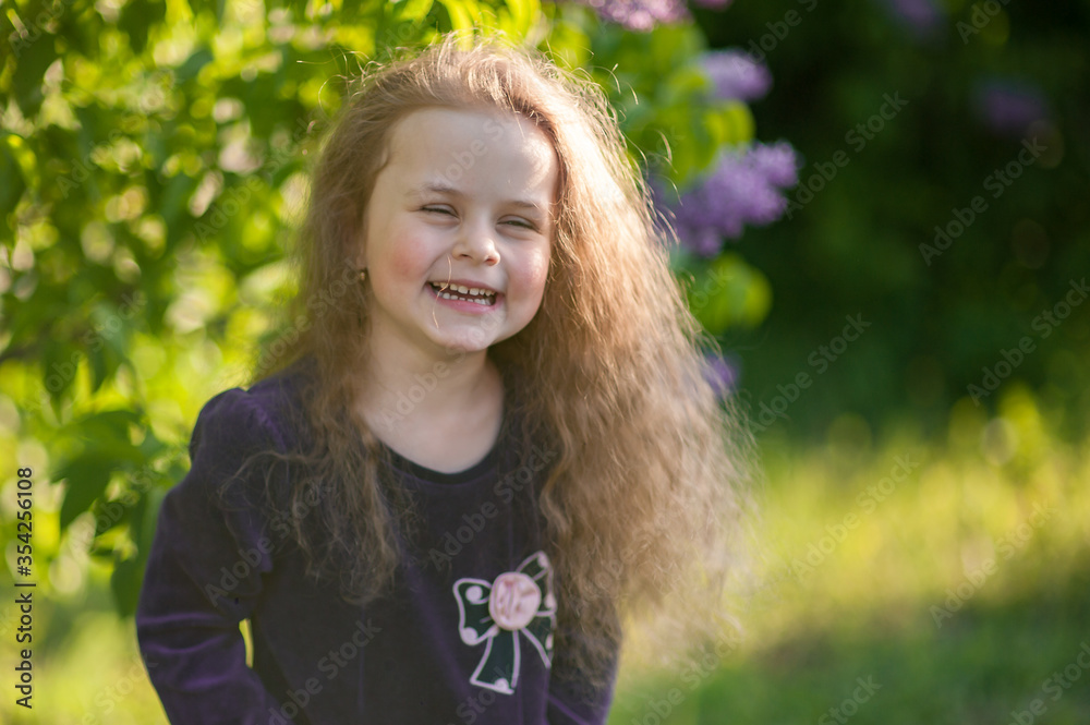 Outside portrait of a beautiful girl with long curly hair near lilac bushes Outside portrait of a beautiful girl with long curly hair near lilac bushes