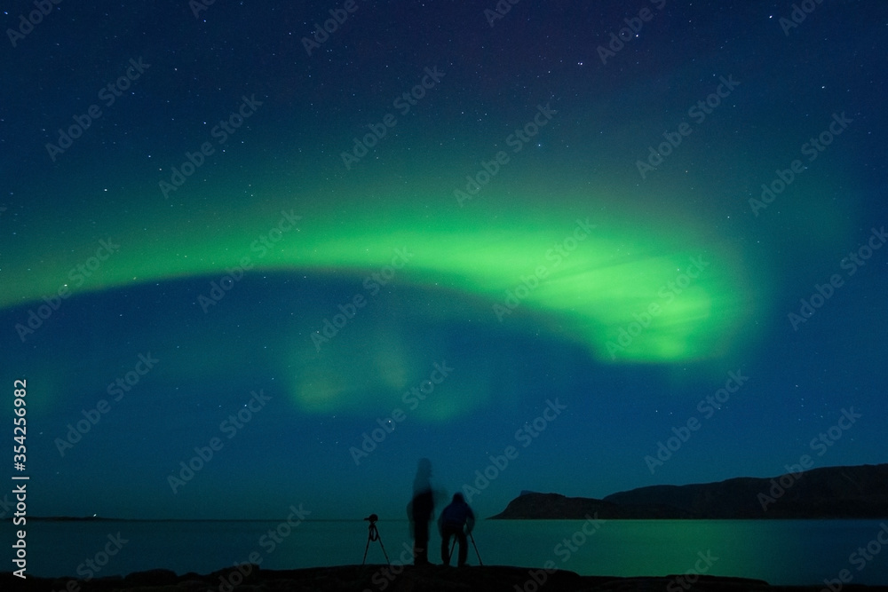 Northern Lights with green bow over the horizon and people trying to take a picture of it.