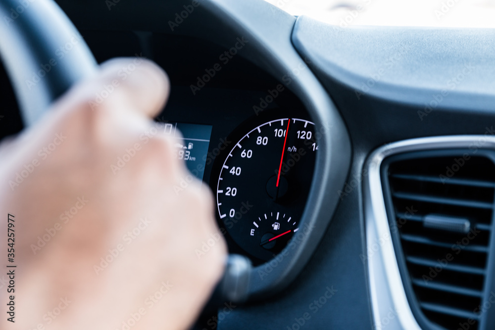 closeup of a hand on steering wheel and speedometer in the background  